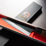 Closeup of the blade of Nishida Hamono Kurouchi Gyuto Knife 165mm in an open box over the cover with Nishida Hamono Japanese character logo