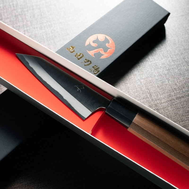 Closeup of the blade of Nishida Hamono Polish Petty Knife 100mm in an open box over the cover with Nishida Hamono Japanese character logo