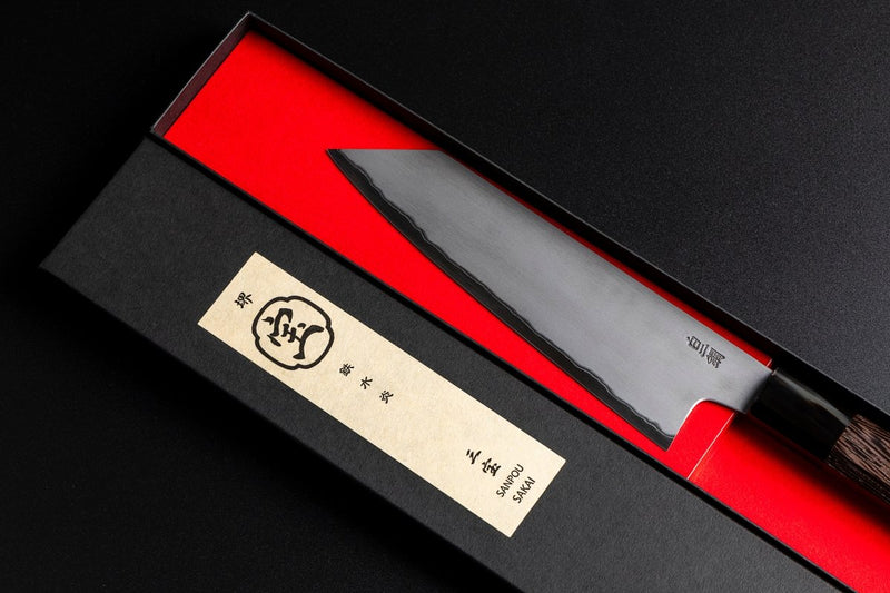 Close-up of the blade of Sakai TAKAYUKI Kiritsuke 180mm by Aoki Hamono inside its box next to the cover with a Japanese characters label in the cover