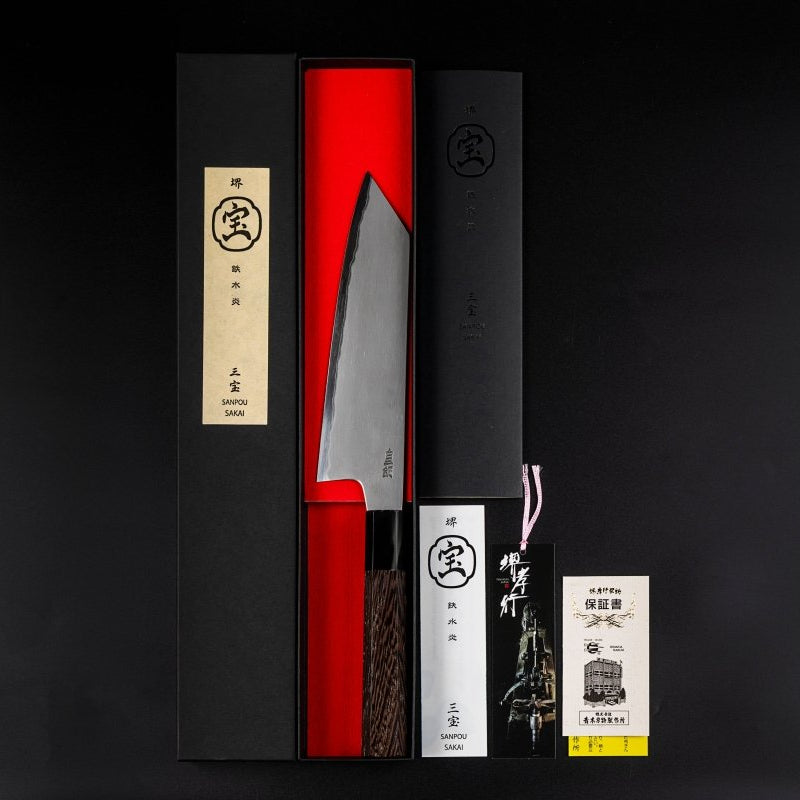 Sakai TAKAYUKI Kiritsuke 180mm by Aoki Hamono inside its red inner box next to its Japanese characters label cover, product instructions card and guaranteee card, all vertically aligned