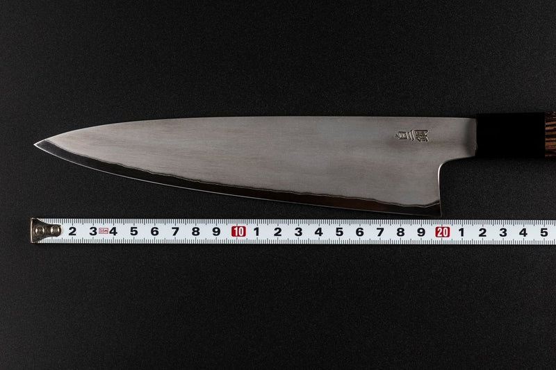 Blade of Sakai TAKAYUKI Gyuto 210mm by Aoki Hamono over a measure tape that shows the length of the blade