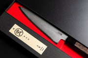 Close-up of the blade of Sakai TAKAYUKI Gyuto 210mm by Aoki Hamono inside its box next to the cover with a Japanese characters label in the cover