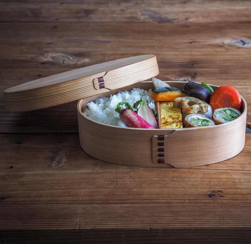 Oval Bento Box crafted by Hakata Bentwood Tamaki filled with rice and vegetables on wooden background