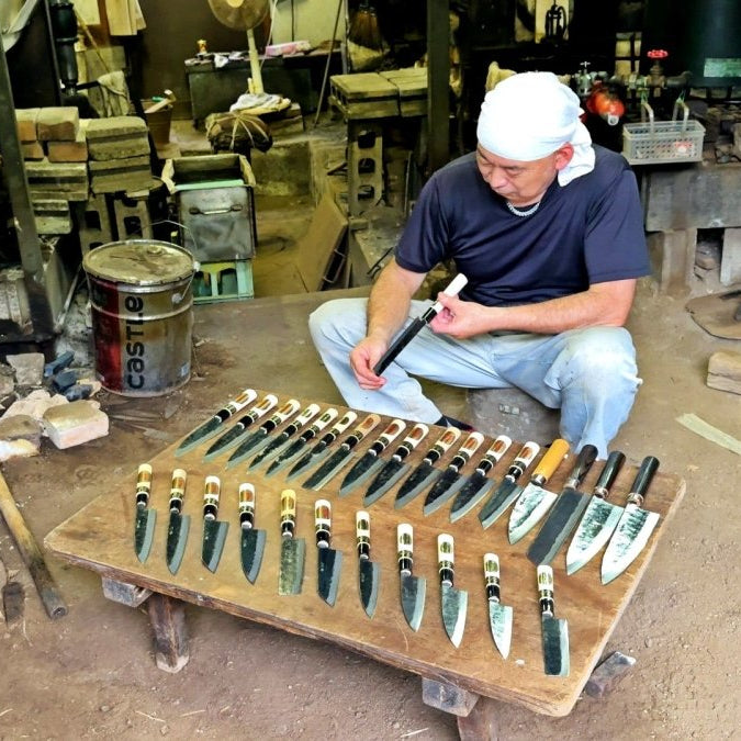 Shigemitsu Hamono master craftsman inspecting a knife in front of a low table full of knives