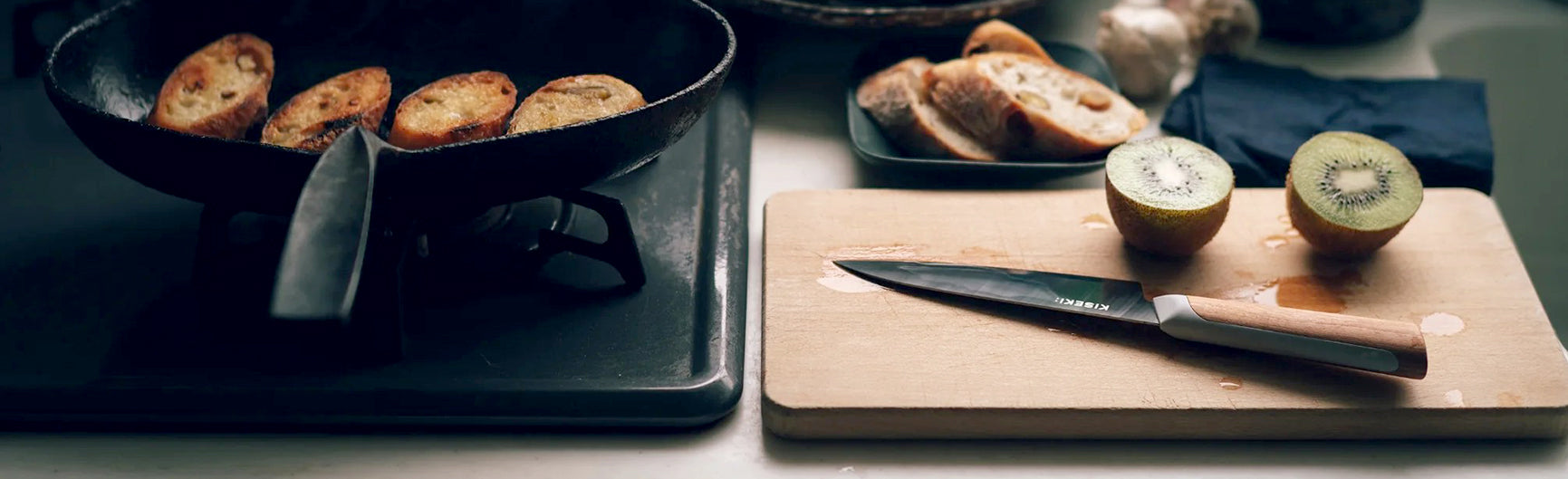 Fry pan with bread next wo a wooden cutting board with 2 halves of a iwi and a KISEKI Petty Knife from Fukuda Hamono