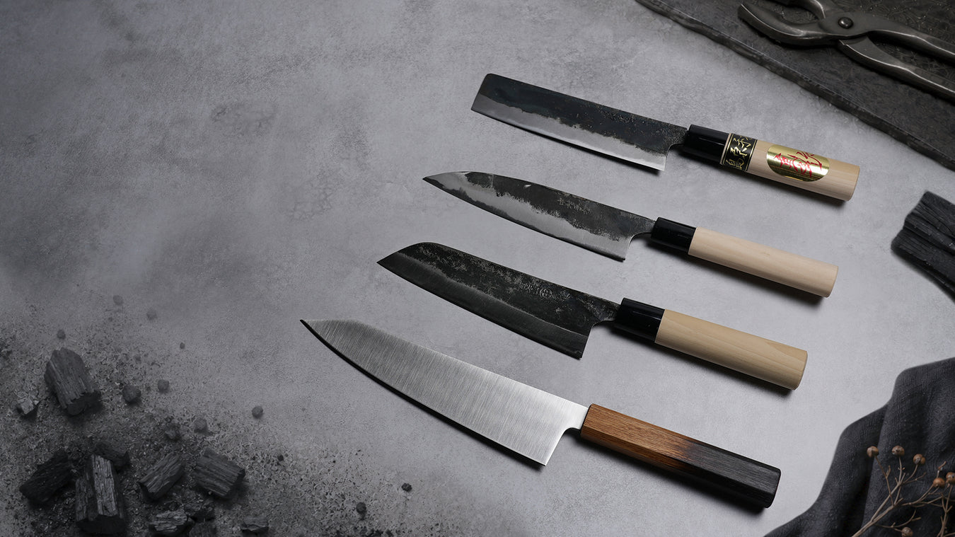 A Inoguchi Hamono kiritsuke knife, two Nakamura Blacksmith santoku knives and a Nakamura Hamono nakiri knife over a grey workshop background