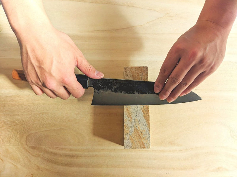 Close up from an above perspective of two hands sharpening a Classic Santoku Kitchen Knife 200mm by Asano Blacksmith over the included free Amakusa Red Sharpening stone