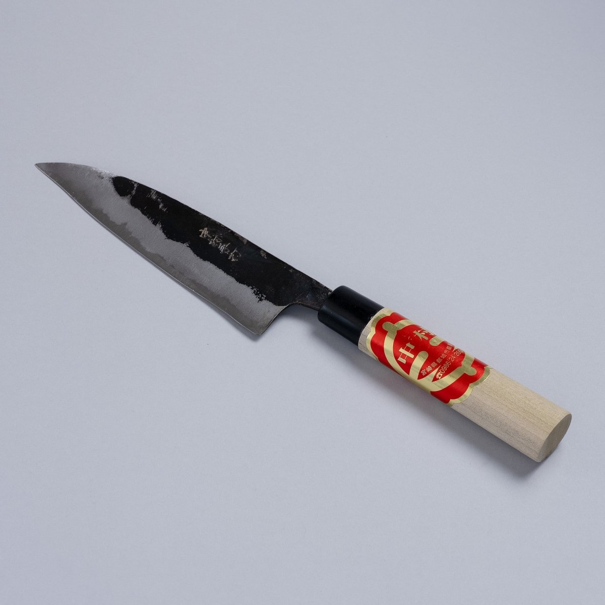 Kurouchi Santoku Knife 150mm crafted by Nakamura Blacksmith displayed diagonally on grey background