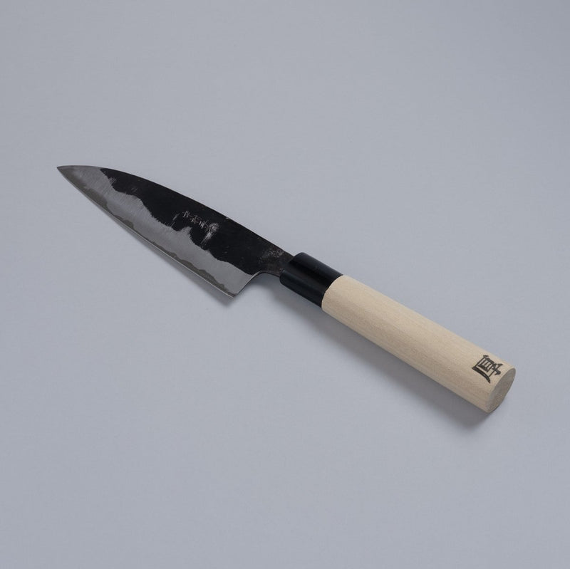 Thick version of Kurouchi Santoku Knife 150mm crafted by Nakamura Blacksmith displayed diagonally on grey background