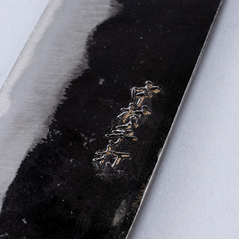 Closeup on engraving on Kurouchi Santoku Knife 150mm crafted by Nakamura Blacksmith on grey background