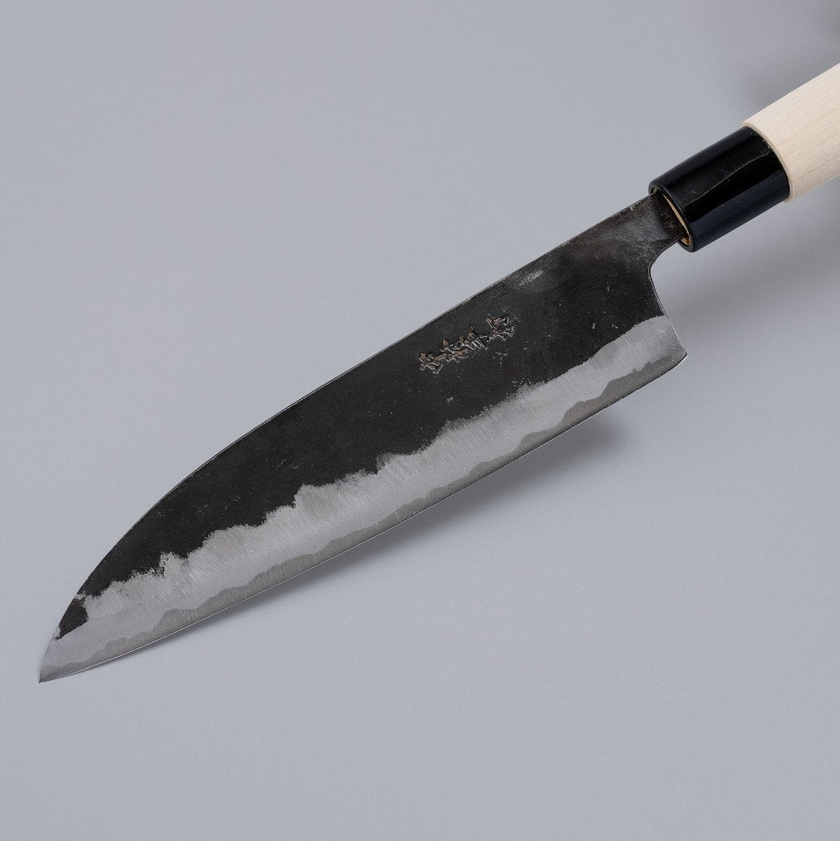 Closeup on tip of Kurouchi Santoku Knife 180mm crafted by Nakamura Blacksmith on grey background