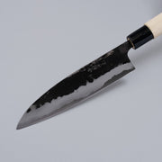 Closeup on tip of Kurouchi Santoku Knife 165mm crafted by Nakamura Blacksmith displayed diagonally on grey background