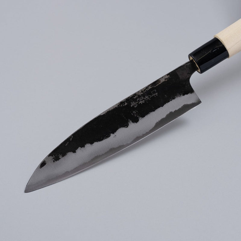 Closeup on tip of Kurouchi Santoku Knife 165mm crafted by Nakamura Blacksmith displayed diagonally on grey background