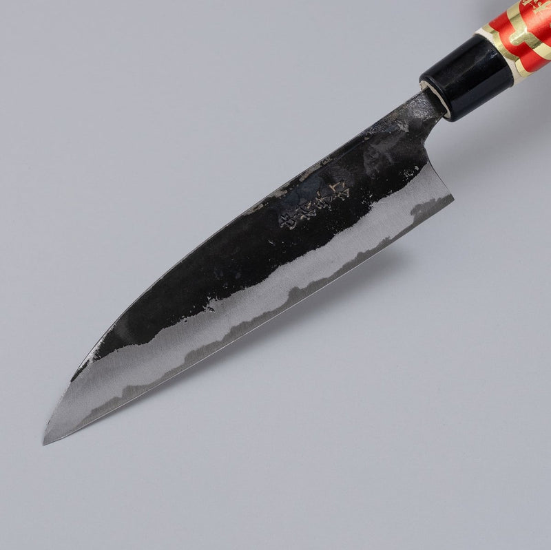 Closeup on tip of Kurouchi Santoku Knife 150mm crafted by Nakamura Blacksmith displayed diagonally on grey background