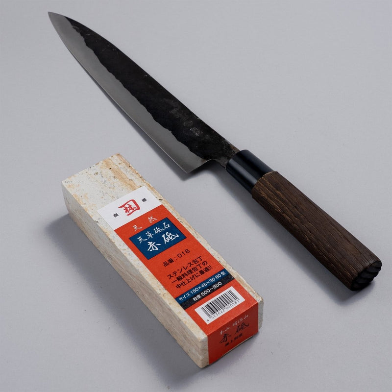 Nakamura Hamono Kurouchi Sashimi Knife 240mm next to the free Amakusa red natural whetstone on a grey background