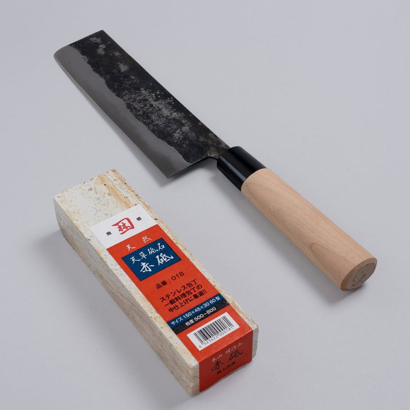 Nakamura Hamono Kurouchi Nakiri Knife 170mm next to the free Amakusa red natural whetstone on a grey background