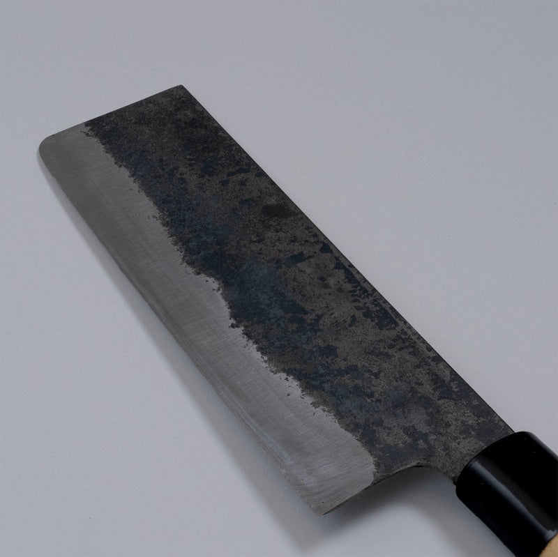Closeup on reverse side of Single-Bevel Kurouchi Nakiri Knife 160mm crafted by Shirou Kunimitsu displayed diagonally on grey background