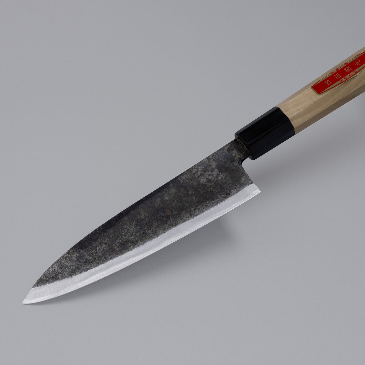 Closeup on tip of special Kurouchi Vegetable Funayuki Knife 170mm crafted by Shirou Kunimitsu displayed diagonally on grey background