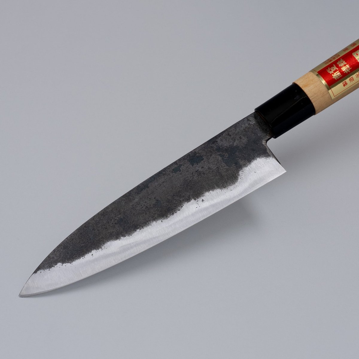 灰色の背景に國光四郎作の片刃黒内三徳包丁 170mm の先端のクローズアップ