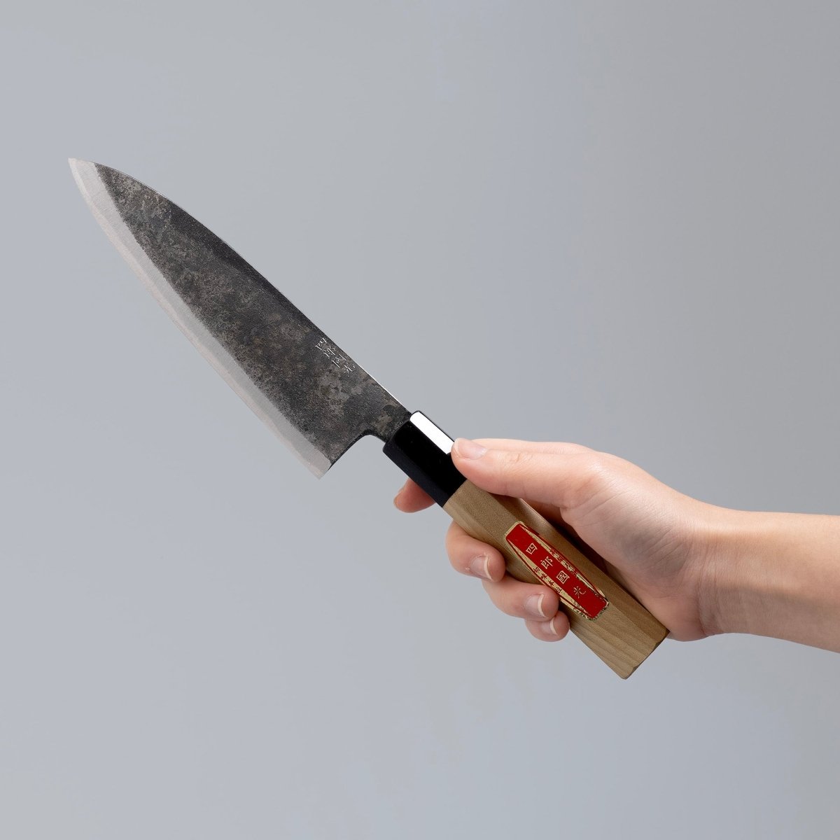 Hand holding special Kurouchi Vegetable Funayuki Knife 170mm crafted by Shirou Kunimitsu on grey background