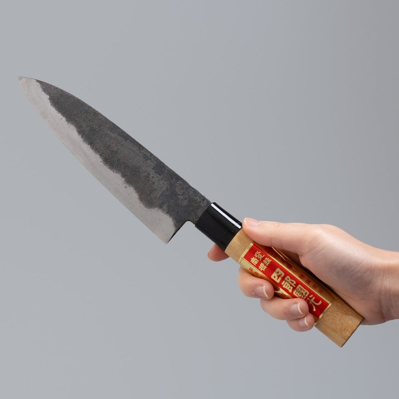 Hand holding single-Bevel Kurouchi Santoku Knife 170mm crafted by Shirou Kunimitsu on grey background