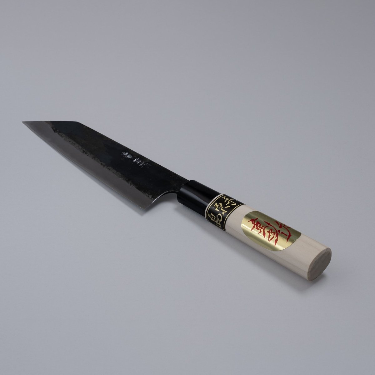 Kurouchi Santoku knife 160mm crafted by Shigemitsu Hamono displayed diagonally on grey background 