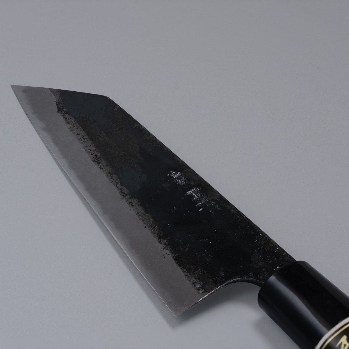 Closeup on blade of Kurouchi Santoku knife 160mm crafted by Shigemitsu Hamono on grey background 
