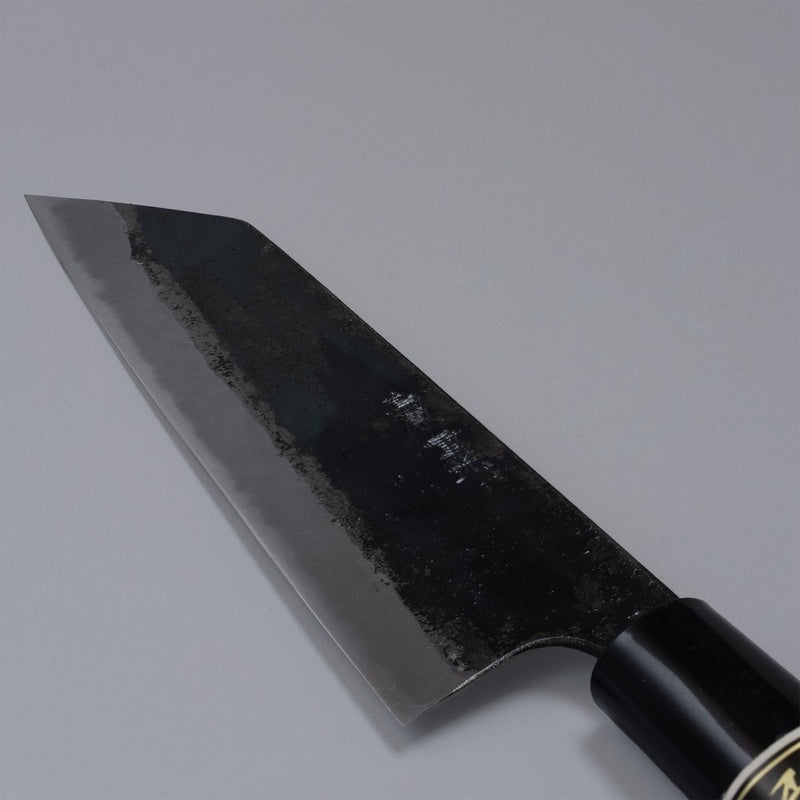Closeup on blade of Kurouchi Santoku knife 160mm crafted by Shigemitsu Hamono on grey background 
