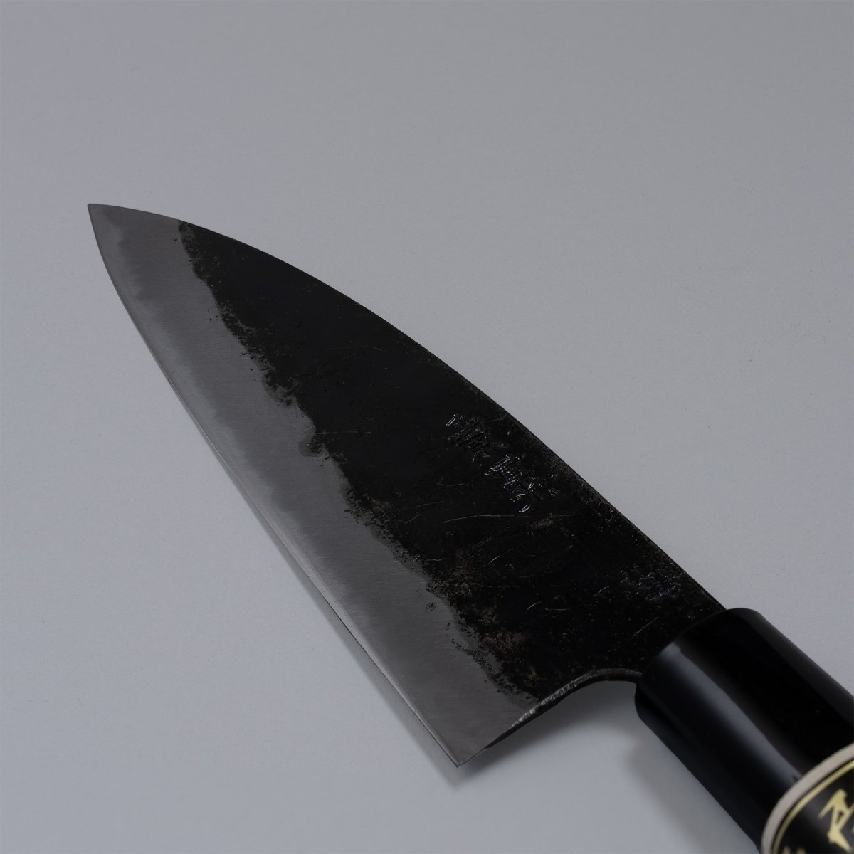 Closeup on blade of Kurouchi Deba knife 155mm crafted by Shigemitsu Hamono on grey background 