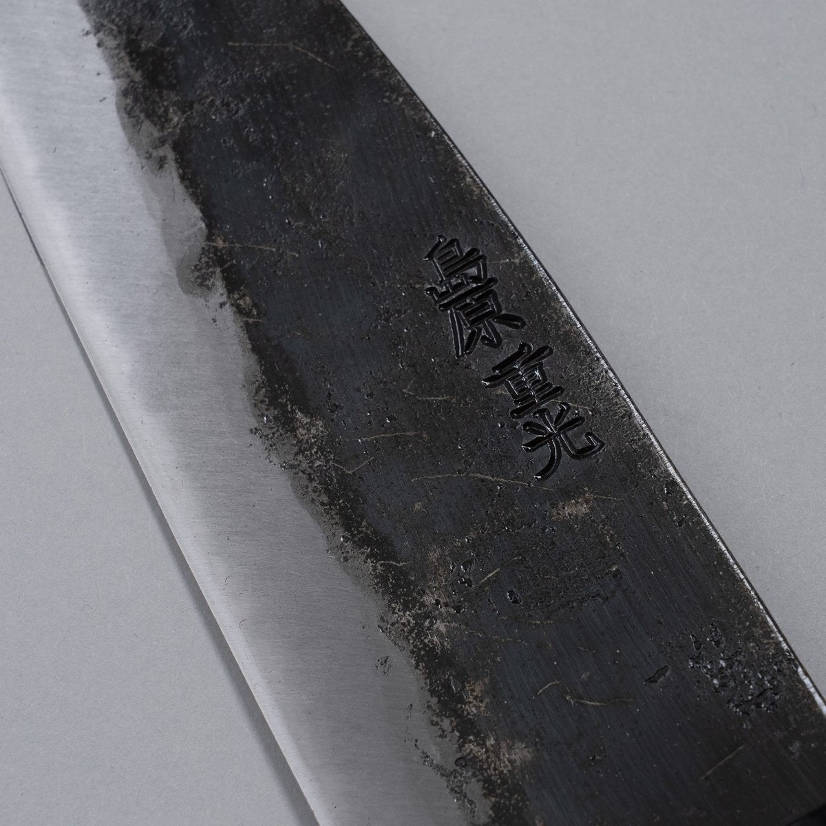 Closeup on engraving on blade of Kurouchi Santoku knife 160mm crafted by Shigemitsu Hamono on grey background 