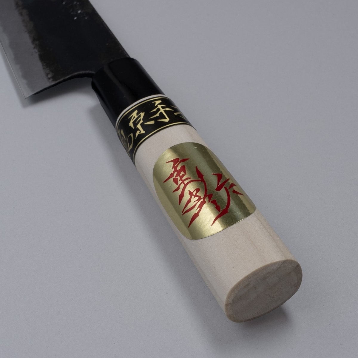 Closeup on handle of Kurouchi Santoku knife 160mm crafted by Shigemitsu Hamono displayed diagonally on grey background 