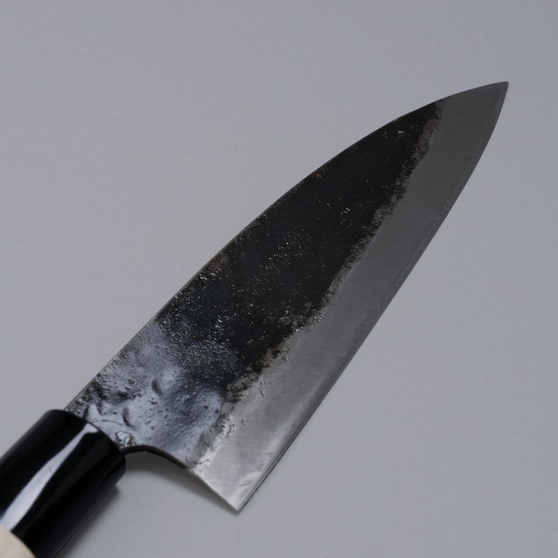 Closeup on blade of Kurouchi Deba knife 155mm crafted by Shigemitsu Hamono displayed diagonally on grey background 