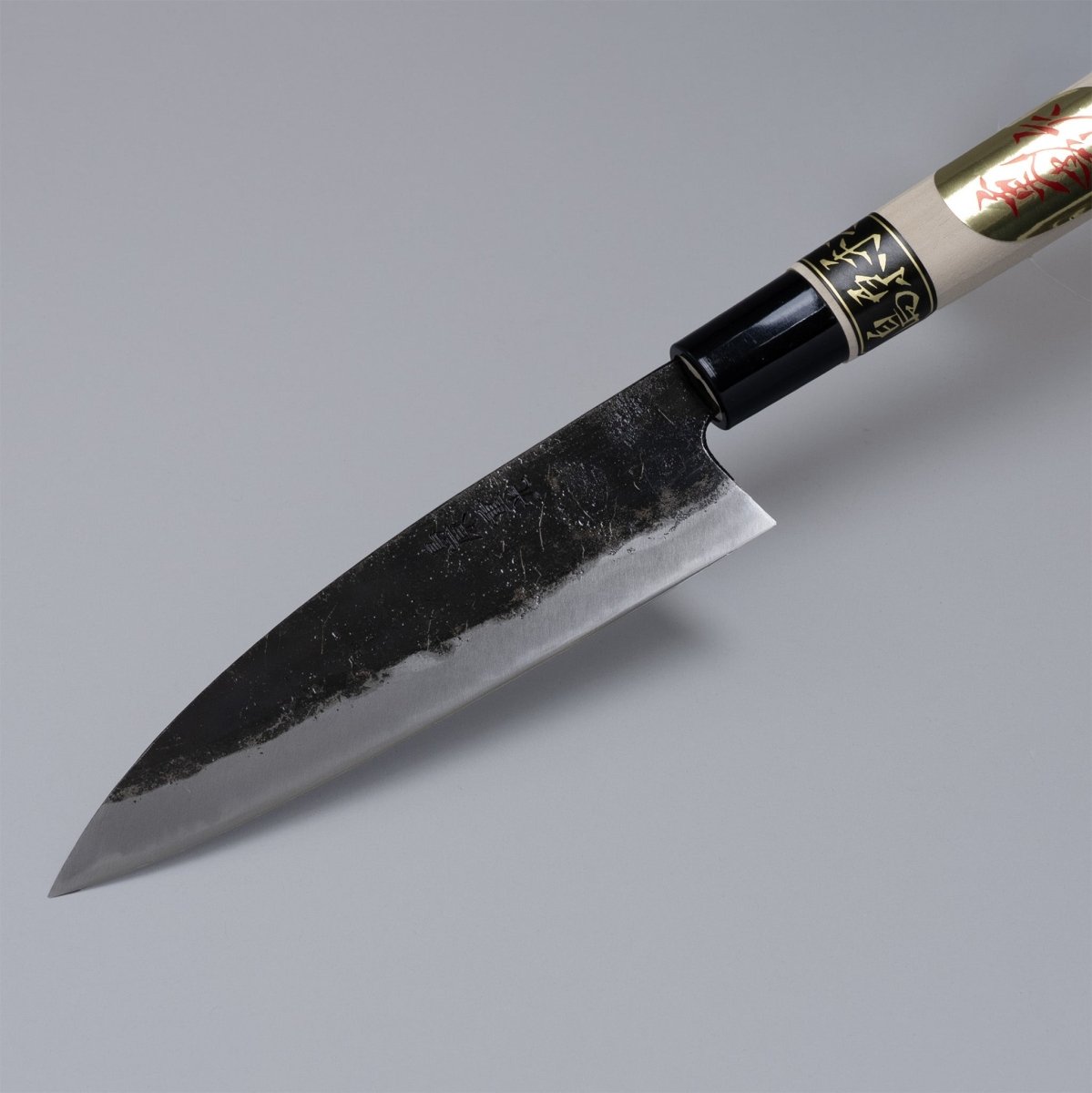 Closeup on tip of Kurouchi Deba knife 155mm crafted by Shigemitsu Hamono on grey background 