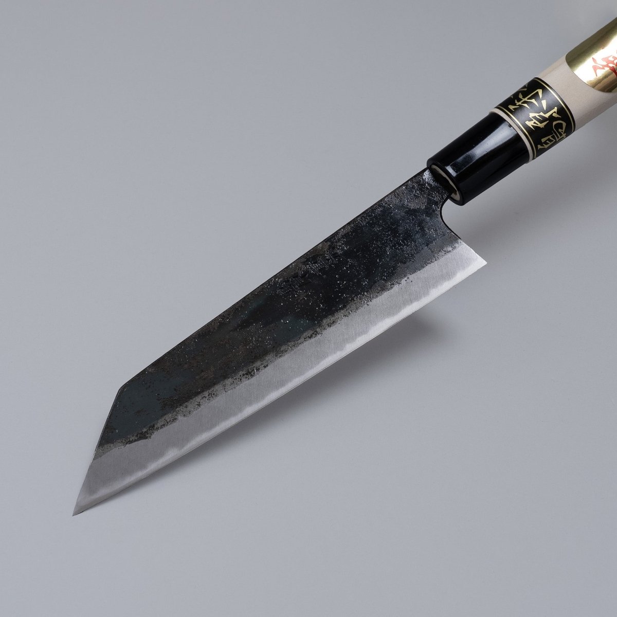 Closeup on tip of Kurouchi Santoku knife 160mm crafted by Shigemitsu Hamono displayed diagonally on grey background 