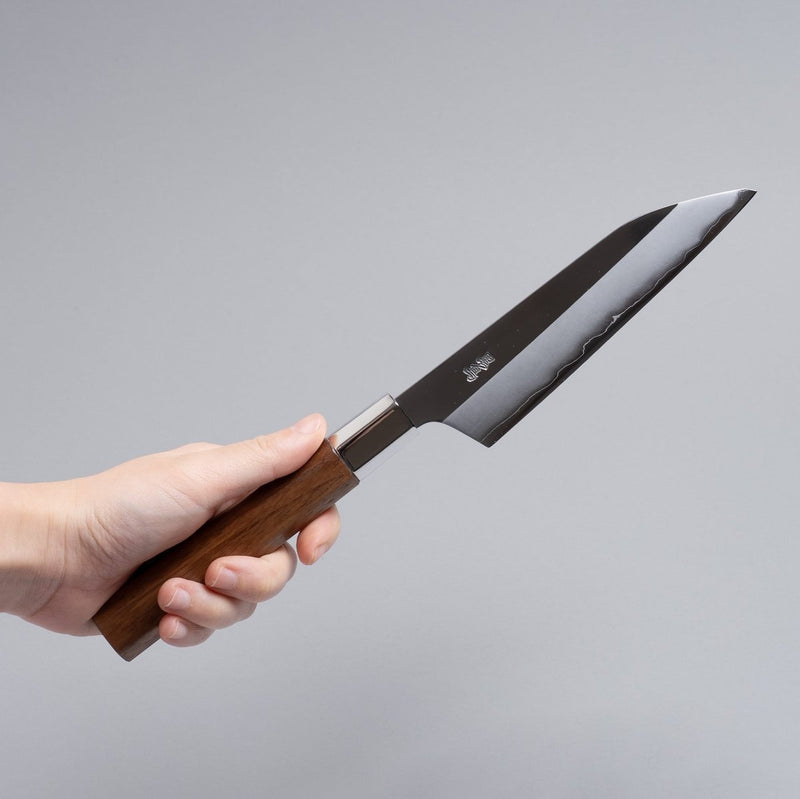 Hand holding ginsan stainless Petty knife 135mm crafted by Kurotori Blacksmith on grey background