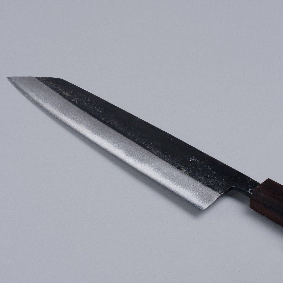 Closeup on blade of Kurouchi Damascus Blue Steel No. 2 Kiritsuke 210mm by Kajihara Hamono displayed diagonally on grey background