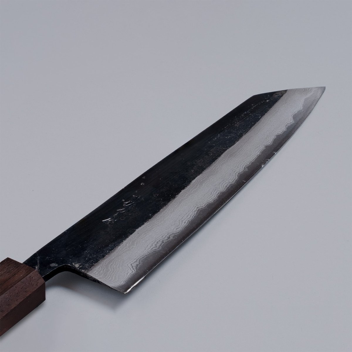 Closup on damascus pattern of Kurouchi Damascus Blue Steel No. 2 Kiritsuke 210mm by Kajihara Hamono displayed diagonally on grey background