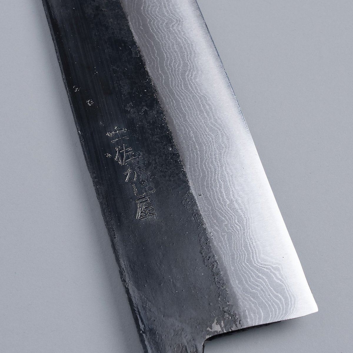 Closeup on engraving on blade of Kurouchi Damascus Blue Steel No. 2 Kiritsuke 210mm by Kajihara Hamono on grey background