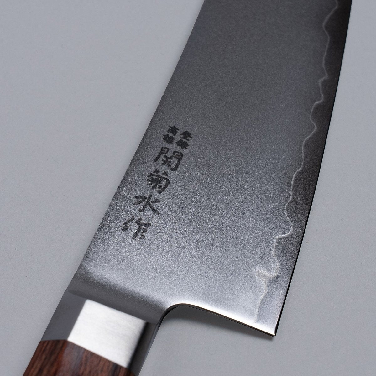 Closeup on manufacturer name on blade of VG-10 stainless steel KIRINAMI Kiritsuke Bunka 150mm crafted by Seki Kikusui Cutlery on grey background