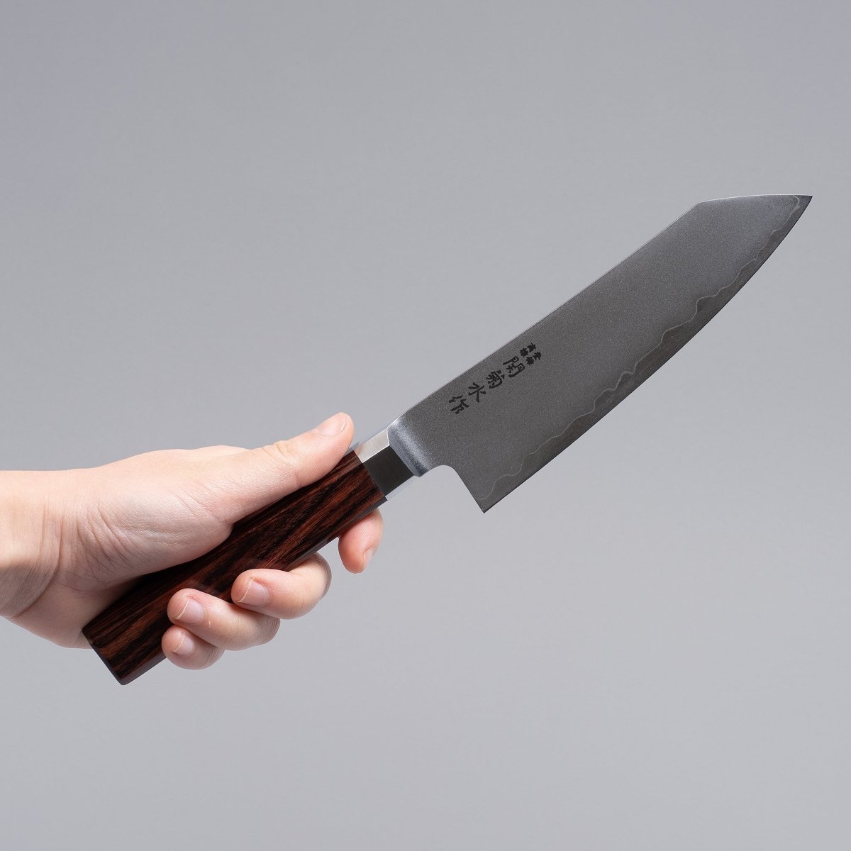 Hand holding VG-10 stainless steel KIRINAMI Kiritsuke Bunka 150mm crafted by Seki Kikusui Cutlery on grey background