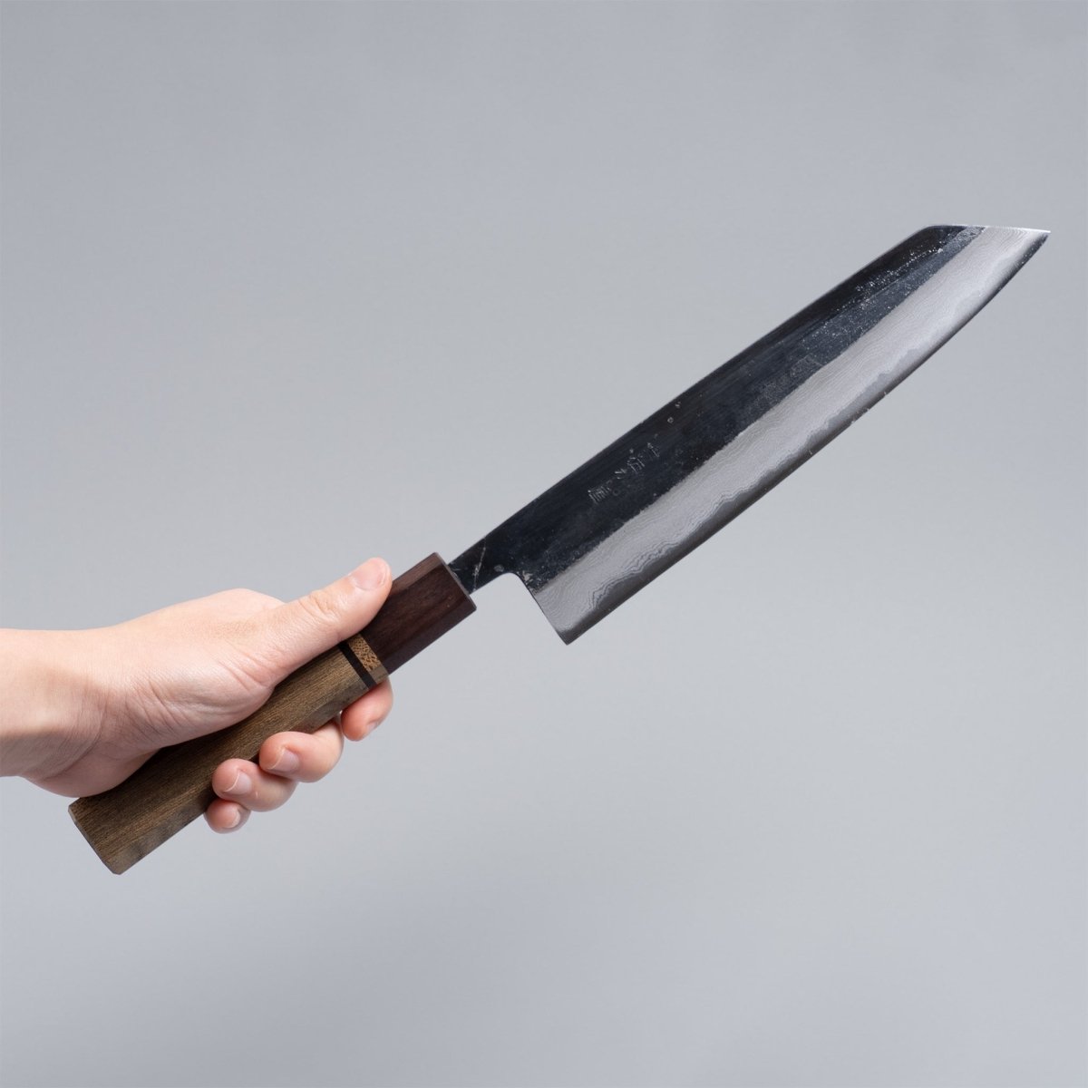 Hand holding Kurouchi Damascus Blue Steel No. 2 Kiritsuke 210mm by Kajihara Hamono on grey background