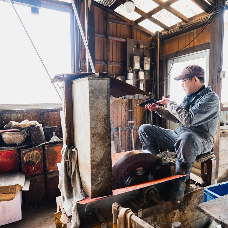 Miwa Hamono master artisan, Hidetoshi Miwa, checking a balde in front of the sharpener tools inside the workshop