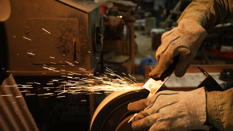 Closeup of Kyohei Shindo's hands in gloves sharpening a blade while sparks fly
