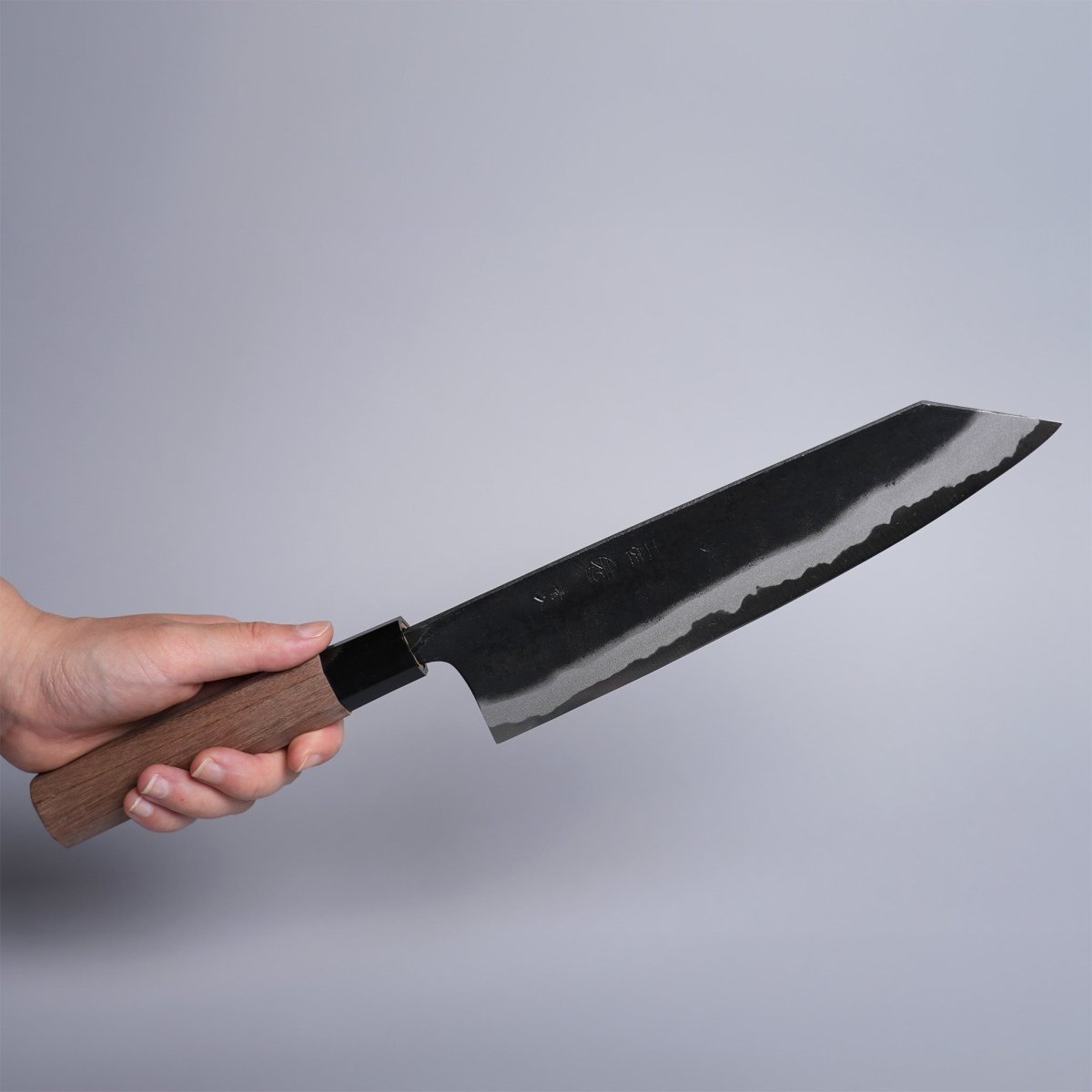 Hand holding Kyohei Shindo Kurouchi Kiritsuke Gyuto 220mm crafted from Aogami 2 in Kochi, Japan on grey background