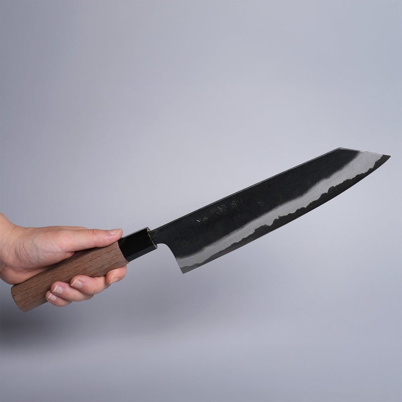 Hand holding Kyohei Shindo Kurouchi Kiritsuke Gyuto 220mm crafted from Aogami 2 in Kochi, Japan on grey background