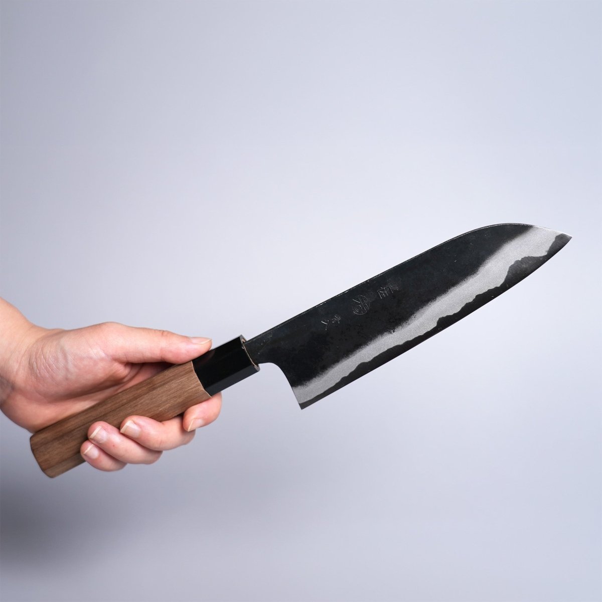 Hand holding Kyohei Shindo Kurouchi Santoku 170mm crafted from Aogami 2 in Kochi, Japan on grey background