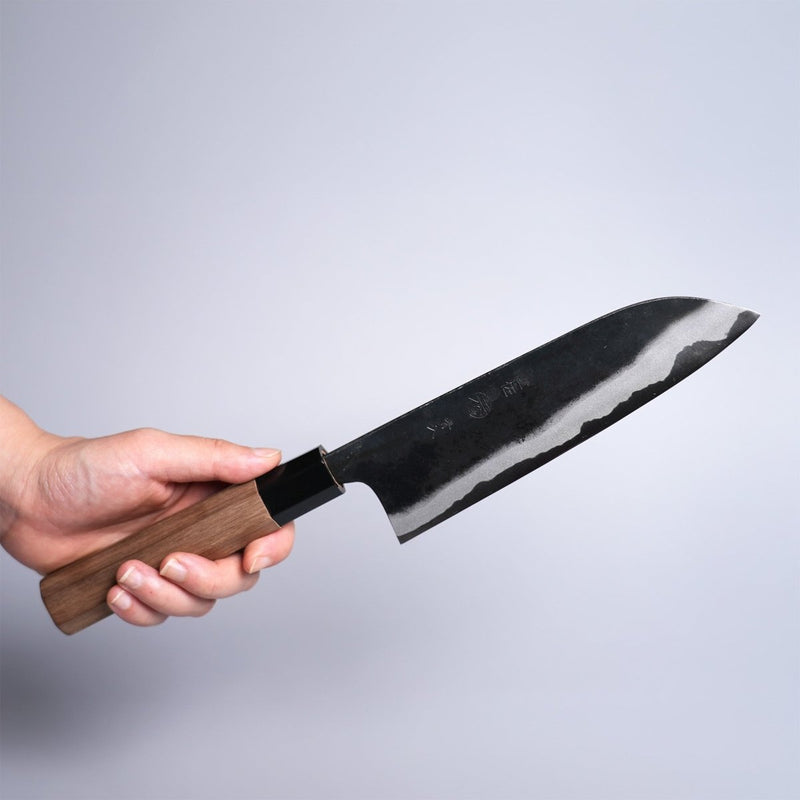 Hand holding Kyohei Shindo Kurouchi Santoku 170mm crafted from Aogami 2 in Kochi, Japan on grey background