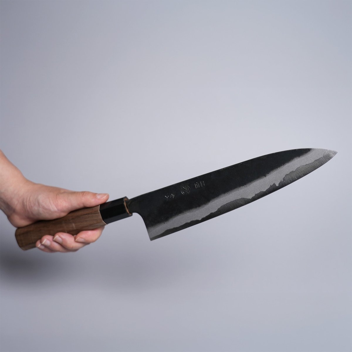 Hand holding Kyohei Shindo Kurouchi Gyuto 220mm crafted from Aogami 2 in Kochi Japan on grey background