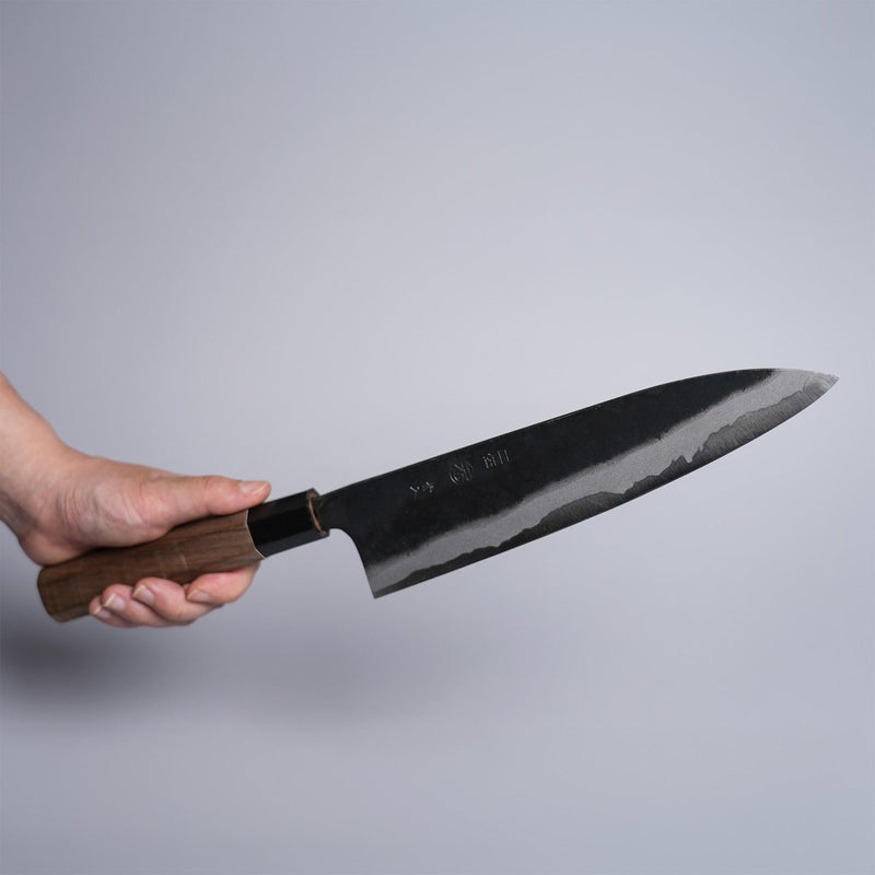 Hand holding Kyohei Shindo Kurouchi Gyuto 220mm crafted from Aogami 2 in Kochi Japan on grey background