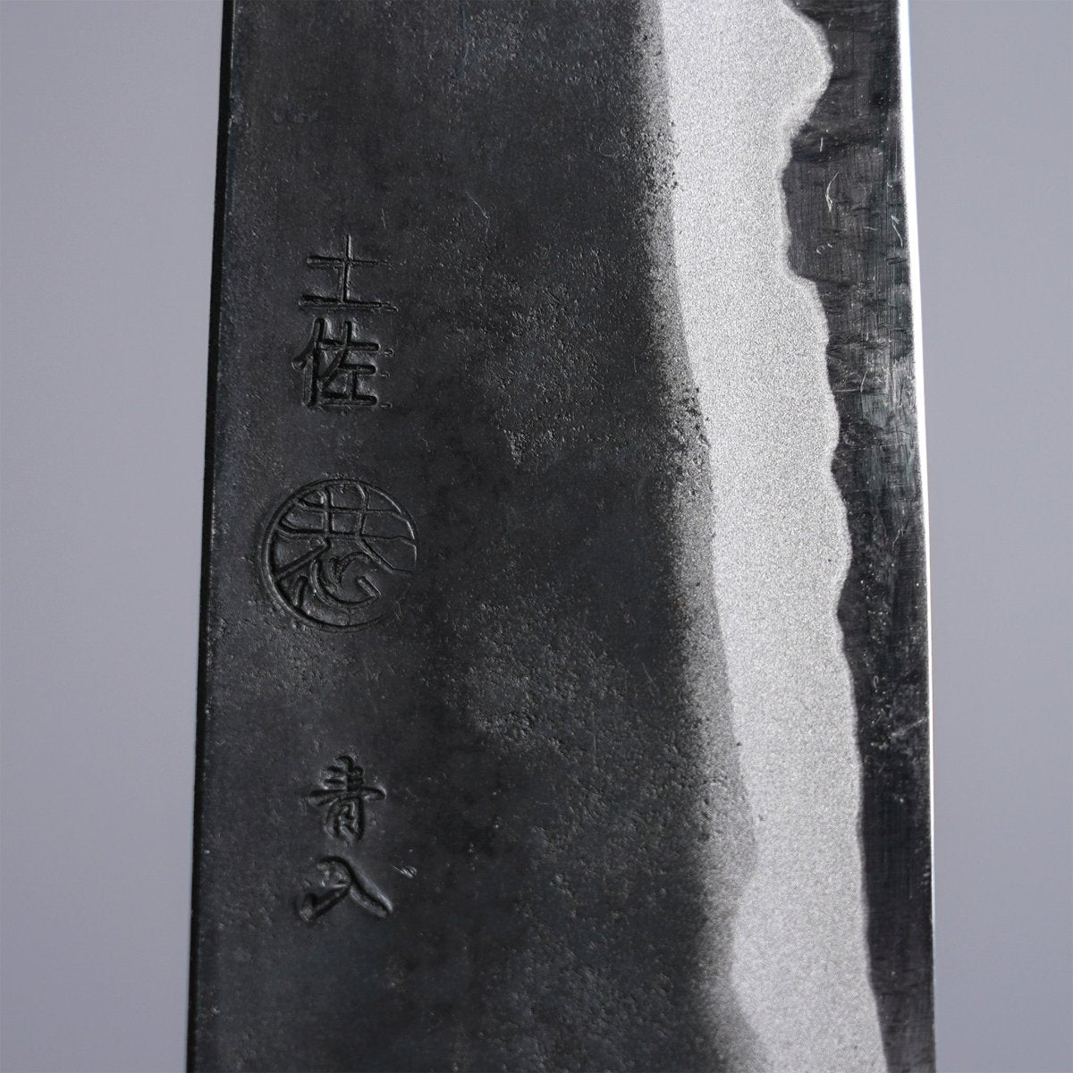 Closeup on engraving on Kyohei Shindo Kurouchi Gyuto 220mm crafted from Aogami 2 in Kochi Japan on grey background